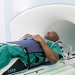 Patient in a green gown moved into an MRI scanner with restraints for a prostate cancer scan