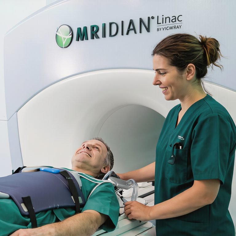 Patient on an MRIdian MRI-Linac table with a radiographer in green scrubs preparing radiotherapy
