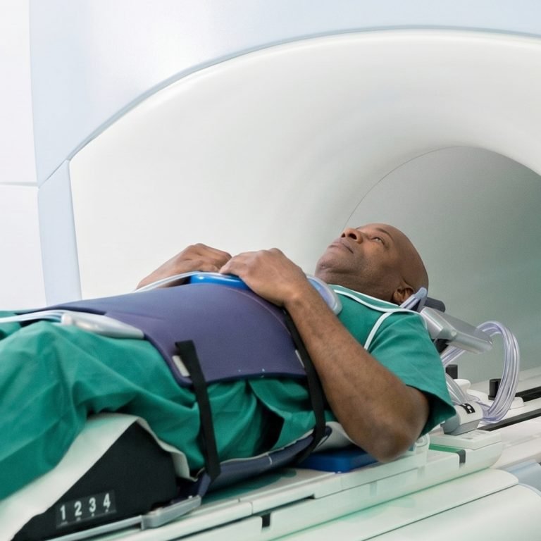 Patient in a green gown moved into an MRI scanner with restraints for a prostate cancer scan