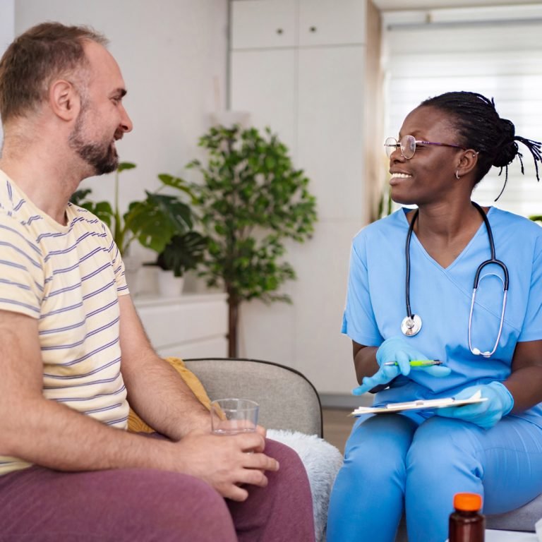 Nurse in blue scrubs talking with a male patient at home during a prostate cancer check-in
