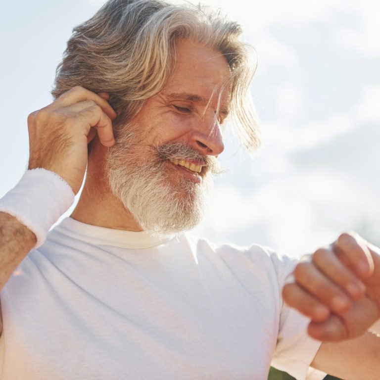 Listening to the music. Senior modern stylish man outdoors on the sportive field at daytime.