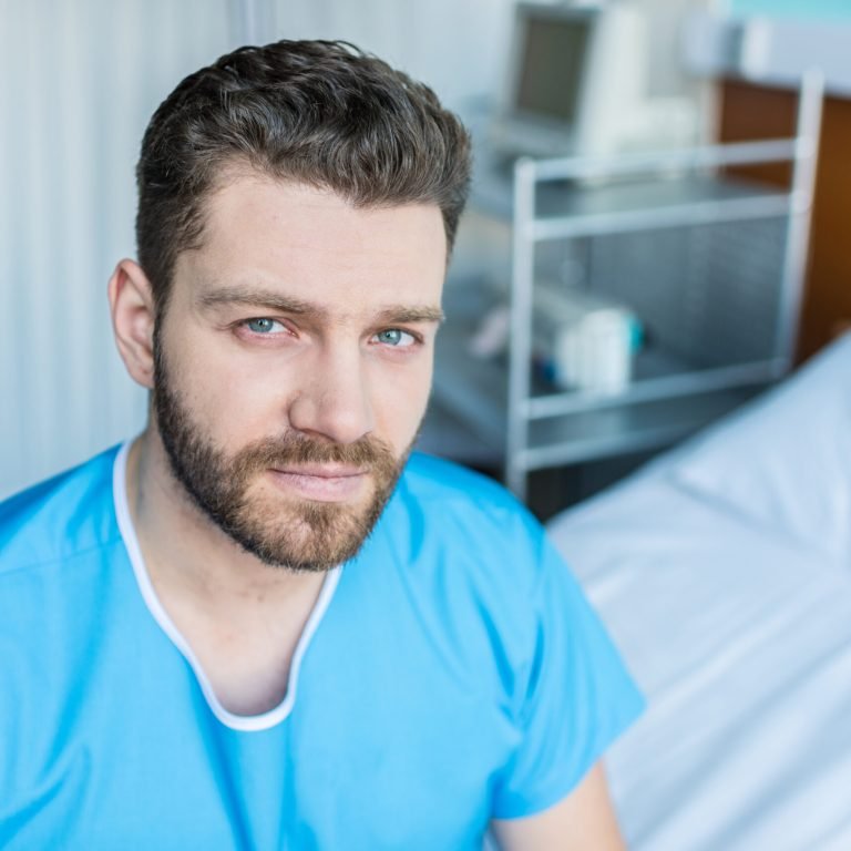Older bearded man sitting on hospital bed receiving prostate cancer care at Surrey oncology clinic